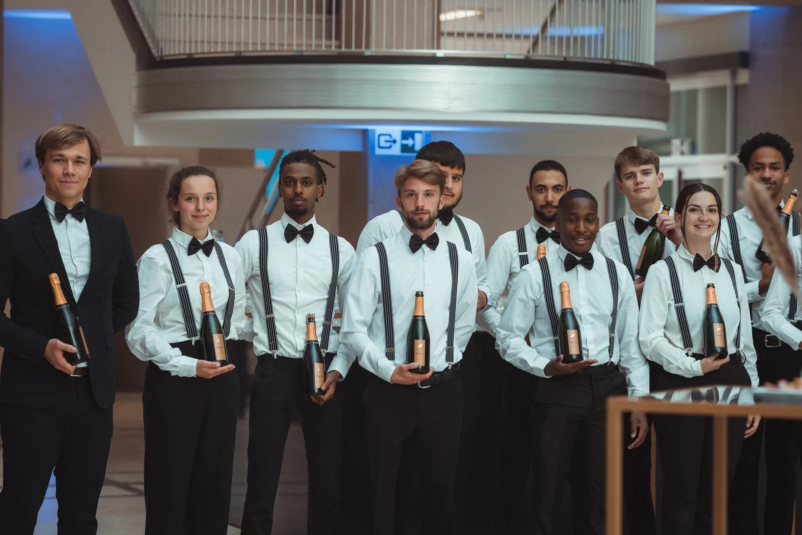 Volledige Studer-crew in wit hemd en vlinderdas met cavaflessen in het atrium van de Nationale Bank